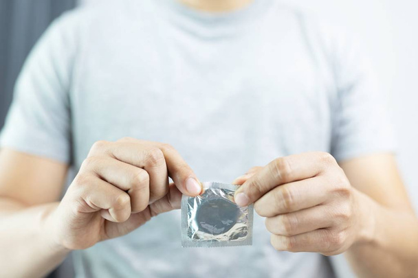 Kondom připravený k použití v mladé mužné ruce, dát kondom bezpečný sexuální koncept na posteli zabránit infekci a antikoncepci kontrolují porodnost nebo bezpečný profylaktické množství. Světový den AIDS, ponechte místo pro text. - Fotografie, Obrázek