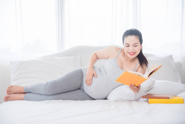 bela ásia grávida mulher deitado no cama e leitura livro
. - Foto, Imagem