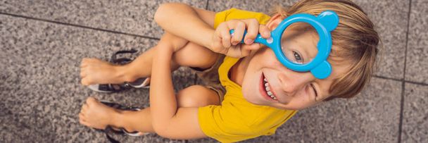 Boy sits on the floor and looks into a magnifying glass BANNER, LONG FORMAT - Photo, image