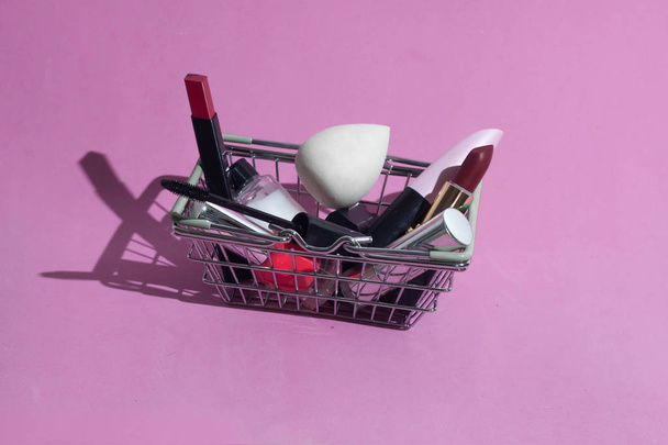 A small basket from the supermarket with makeup products. Decorative cosmetics. On a pink background. - Photo, image