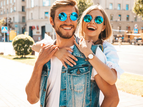 Smiling beautiful girl and her handsome boyfriend. Woman in casual summer dress and man in jeans clothes. Happy cheerful family. Female having fun on the street background.Hugging couple in sunglasses - Foto, afbeelding