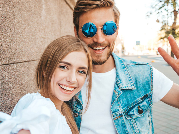 Smiling beautiful girl and her handsome boyfriend in casual summer clothes.Happy family taking selfie self portrait of themselves on smartphone camera in sunglasses.Having fun on the street background  - Фото, изображение