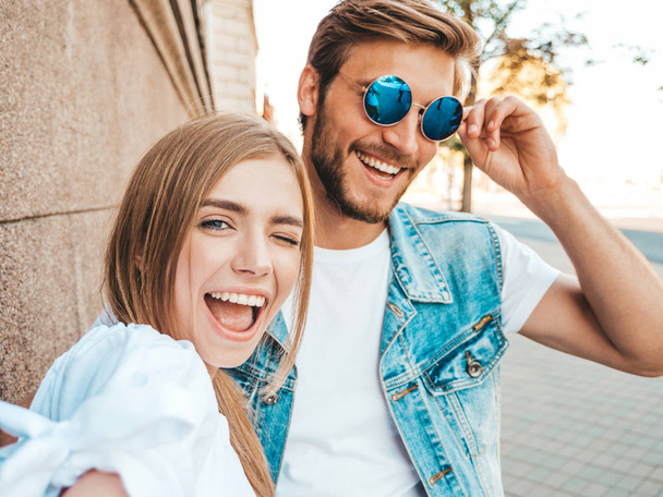 Smiling beautiful girl and her handsome boyfriend in casual summer clothes.Happy family taking selfie self portrait of themselves on smartphone camera in sunglasses.Having fun on the street background  - Fotó, kép