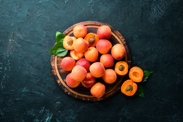 Fresh apricots with green leaves on a black background. Rustic style. Top view. Free space for your text. - Fotó, kép