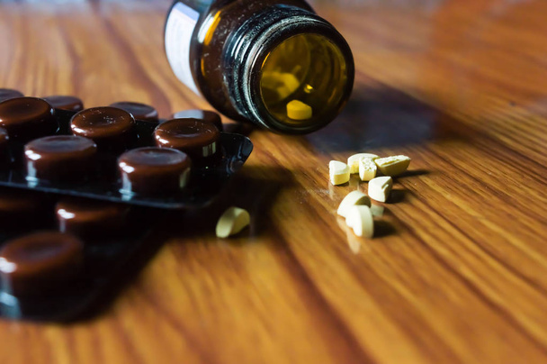 木製のテーブルの背景に薬の丸薬や錠剤のブリスターパックで開く透明なガラスボトルを閉じます。薬局の治療と健康の概念。選択フォーカス浅い被写界深度。自然光. - 写真・画像