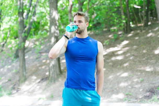 The water has a major role in sports. Thirsty sportsman drinking pure water on hot summer day. Fit athlete having a drink from water bottle during training outdoor. Keeping body water balance - Foto, immagini
