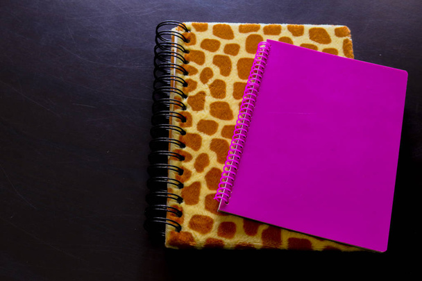 Detail van een luipaard print notebook en roze notebook met de zwarte achtergrond bekeken van bovenaf, Office-objecten - Foto, afbeelding