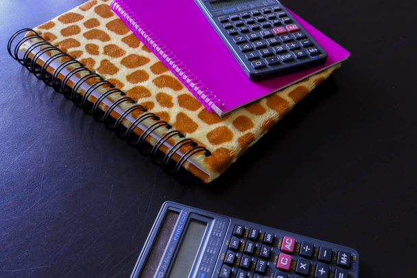 Dos cuadernos y dos calculadoras con el fondo negro visto desde arriba, objetos de oficina
 - Foto, Imagen