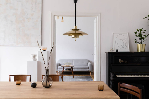 Stylish scandi interior of living room with design wooden table, chairs, sofa, piano and gold pendant lamp. Sitting room with design accessories. Abstract paintings on the wall. Elegant home decor. - Foto, afbeelding