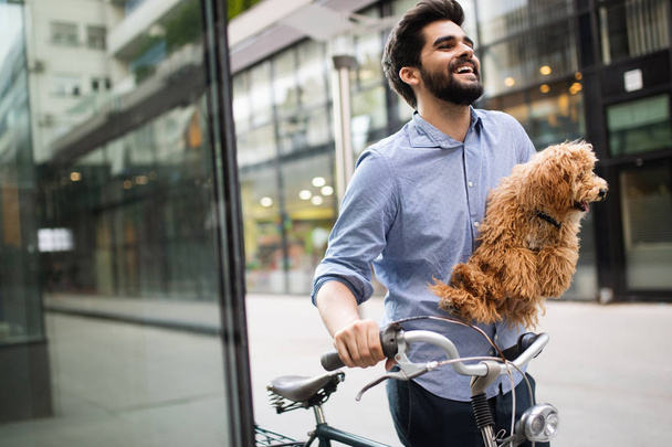 Szczęśliwy przystojny mężczyzna trzyma psa w rękach na zewnątrz w mieście - Zdjęcie, obraz