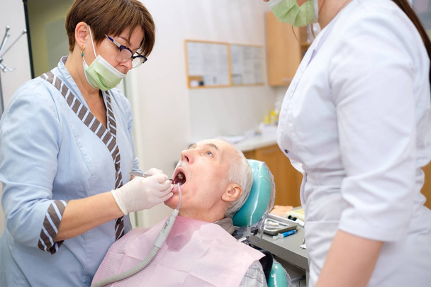 Zahnarzt und Krankenschwester machen professionelle Zahnreinigung männlichen Senior-Patienten in der Zahnarztpraxis. Zahnpflege für ältere Menschen. Zahnmedizin, Medizin und Gesundheitswesen - Foto, Bild
