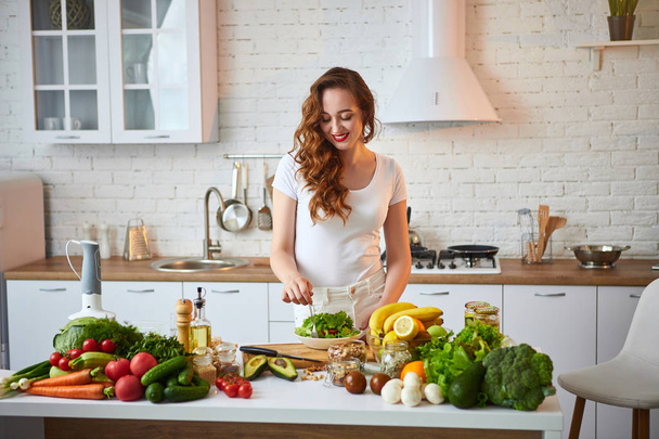 Young happy woman eating salad in the beautiful kitchen with green fresh ingredients indoors. Healthy food concept - Foto, immagini