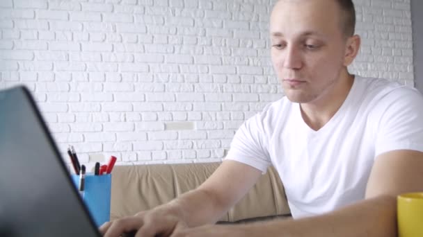 Молодий концентрований білий чоловік стукає на ноутбук, п'ючи з жовтої чашки. Концепція позаштатна робота, бізнес, комунікація, навчання
.  - Кадри, відео