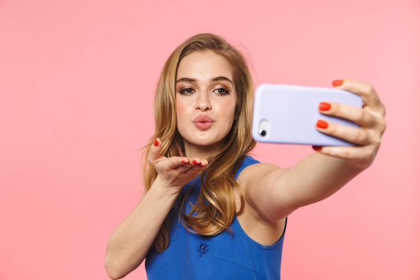 Excited young pretty woman posing isolated over pink wall background take a selfie by phone. - Фото, изображение