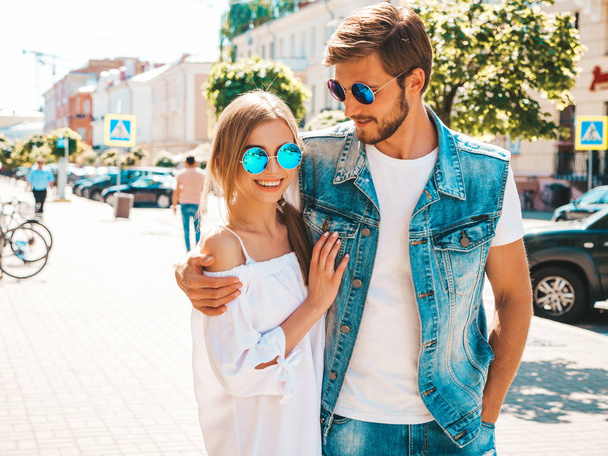 Smiling beautiful girl and her handsome boyfriend walking in the street. Woman in casual summer dress and man in jeans clothes. Happy cheerful couple family having fun in sunglasses - Foto, afbeelding