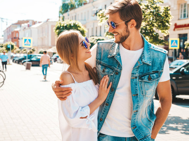 Smiling beautiful girl and her handsome boyfriend walking in the street. Woman in casual summer dress and man in jeans clothes. Happy cheerful couple family having fun in sunglasses - Φωτογραφία, εικόνα