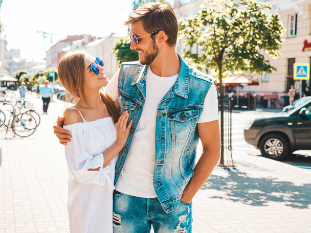 Smiling beautiful girl and her handsome boyfriend walking in the street. Woman in casual summer dress and man in jeans clothes. Happy cheerful couple family having fun in sunglasses - Foto, imagen