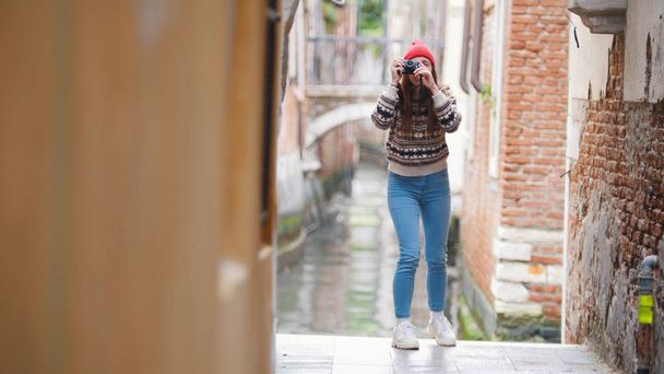 Młoda kobieta stojąca w pobliżu kanału wodnego i zrobiąca zdjęcie na kamerze-Wenecja, Włochy - Zdjęcie, obraz