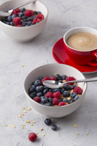 Coffee, bowl of oat flakes with blueberries and raspberries on concrete background. - Photo, Image