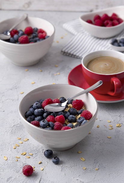 Coffee, bowl of oat flakes with blueberries and raspberries on concrete background. - Foto, afbeelding