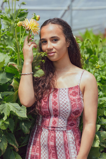 Mujer joven de raza mixta se encuentra en un invernadero de flores en una granja
 - Foto, Imagen