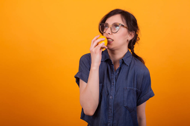 Porträt einer niedlichen jungen Frau, die mit Orange in der Hand vor gelbem Hintergrund im Studio ausrastet - Foto, Bild