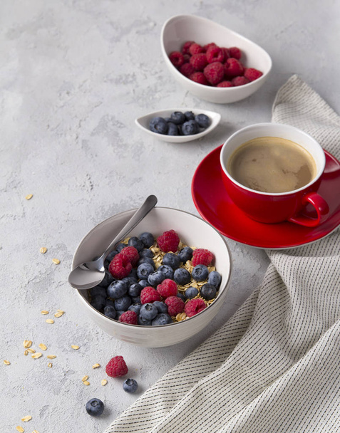 Coffee, bowl of oat flakes with blueberries and raspberries on concrete background. - Foto, immagini