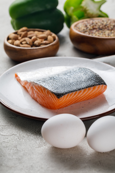 selective focus of fresh raw salmon on white plate near nuts and eggs, ketogenic diet menu - Photo, Image