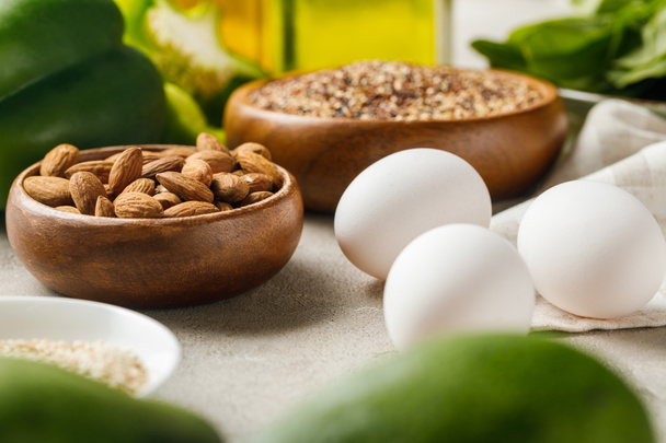 selective focus of nuts in bowls among green vegetables and eggs, ketogenic diet menu - Foto, imagen