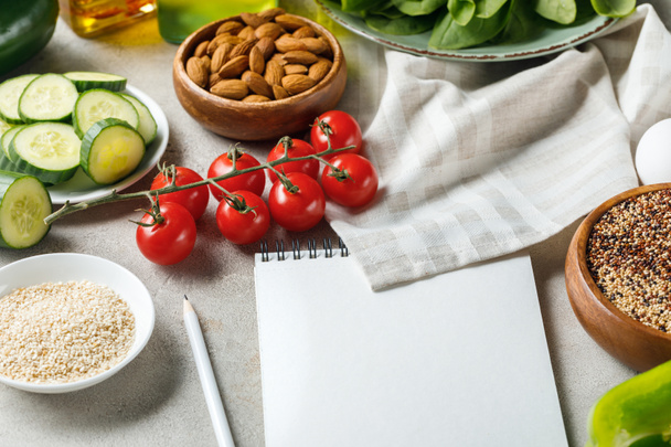 empty notebook with pencil on grey textured surface near napkin, nuts, tomatoes and cucumber, ketogenic diet menu - Photo, Image