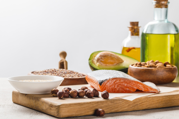 fresh salmon, nuts and avocado on wooden chopping board near oil isolated on grey, ketogenic diet menu - Photo, Image