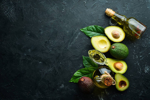 Avocado oil and fresh avocados on a black background. Rustic style. Top view. Free space for your text. - Foto, Bild