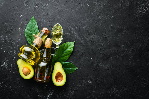 Avocado oil and fresh avocados on a black background. Rustic style. Top view. Free space for your text. - Foto, Imagen