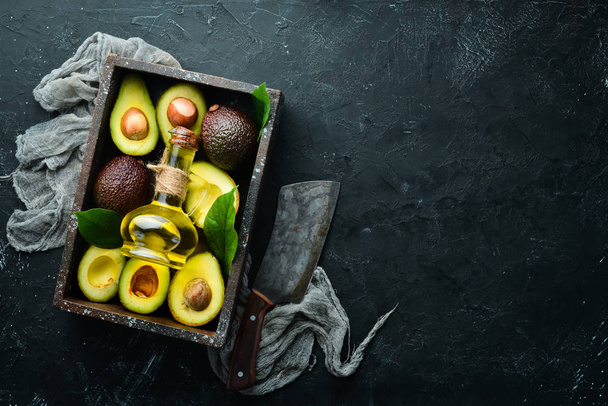 Avocado oil and fresh avocados on a black background. Rustic style. Top view. Free space for your text. - Foto, immagini