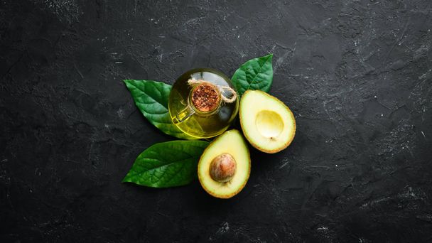 Avocado oil and fresh avocados on a black background. Rustic style. Top view. Free space for your text. - Valokuva, kuva