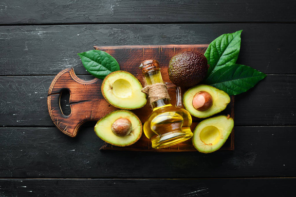 Avocado oil and fresh avocados on a black background. Rustic style. Top view. Free space for your text. - Φωτογραφία, εικόνα