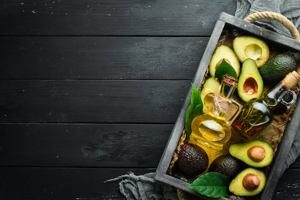 Avocado oil and fresh avocados on a black background. Rustic style. Top view. Free space for your text. - 写真・画像