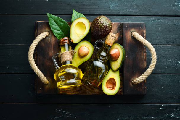Avocado oil and fresh avocados on a black background. Rustic style. Top view. Free space for your text. - Foto, Bild