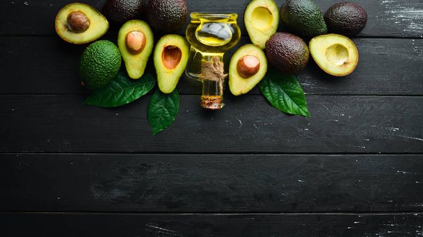 Avocado-olie en verse avocado's op een zwarte achtergrond. Rustieke stijl. Bovenaanzicht. Vrije ruimte voor uw tekst. - Foto, afbeelding