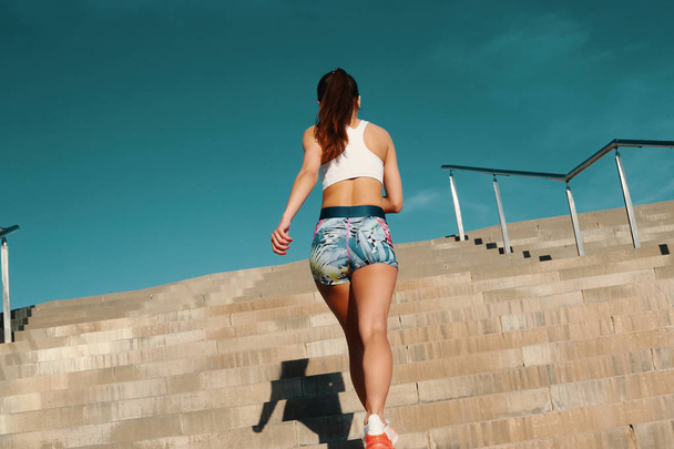 Rear view of beautiful young woman in sports clothing running while exercising outdoors - Valokuva, kuva