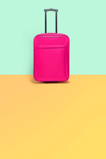 Valigia rosa in piedi accanto alla parete color pastello. Viaggi con
 - Foto, immagini
