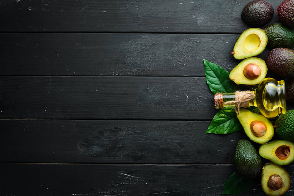 Avocado oil and fresh avocados on a black background. Rustic style. Top view. Free space for your text. - Foto, Imagen