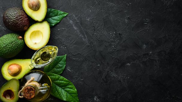 Avocado oil and fresh avocados on a black background. Rustic style. Top view. Free space for your text. - Фото, изображение