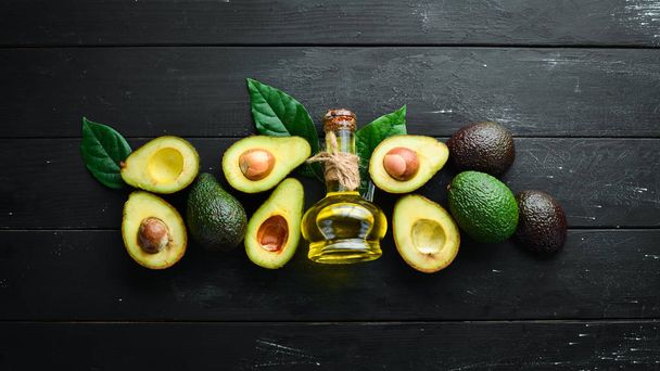 Avocado oil and fresh avocados on a black background. Rustic style. Top view. Free space for your text. - Φωτογραφία, εικόνα