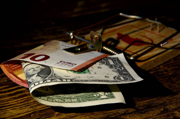 In een houten muizenval is er een Bill van tien euro en een dollar tegen een donkere achtergrond. Concept-riskante financiële transacties, fraude, riskante investeringen. " Er is niet zoiets als een gratis lunch."  - Foto, afbeelding