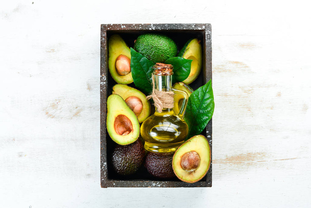 Avocado and avocado oil on a white wooden background. Rustic style. Top view. Free space for your text. - Foto, Imagen
