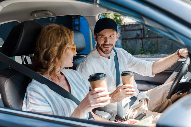 selective focus of cheerful man and woman holding paper cups in car  - Foto, Bild
