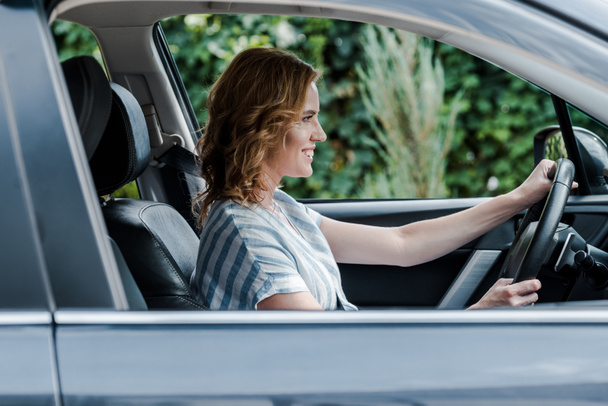 selective focus of cheerful blonde woman driving automobile  - Foto, imagen