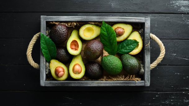 Avocado with leaves in the box. Rustic style. Top view. Free space for your text. - Foto, afbeelding