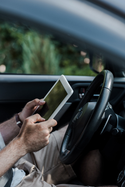 cropped view of man holding digital tablet and sitting in car  - Foto, afbeelding